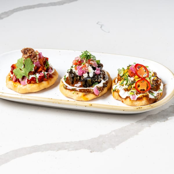 Three vibrant La Prensa Tacos & Tapas sopes, each with unique toppings, on a white platter.