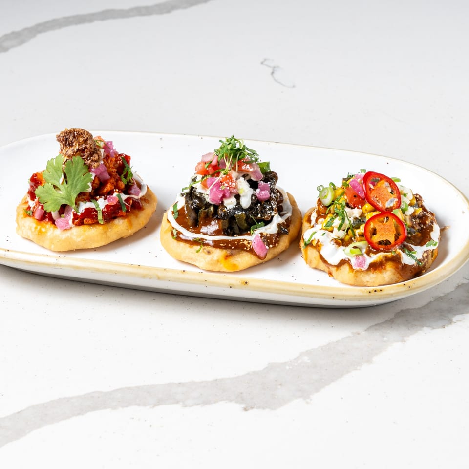 Three vibrant La Prensa Tacos & Tapas sopes, each with unique toppings, on a white platter.