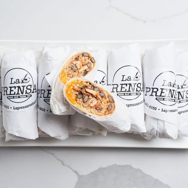 A tray of La Prensa burritos, one cut in half revealing chicken, beans, and cheese.