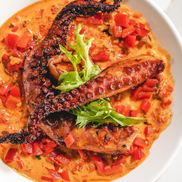 Grilled octopus tentacles in a creamy orange sauce with diced red peppers and green garnish.