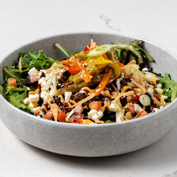 A La Prensa Tacos & Tapas bowl with seasoned meat, peppers, cheese, tomatoes, and greens.