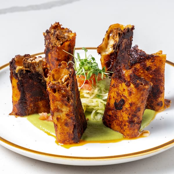 Five crispy La Prensa Tacos & Tapas taquitos stand in green sauce with a side salad.
