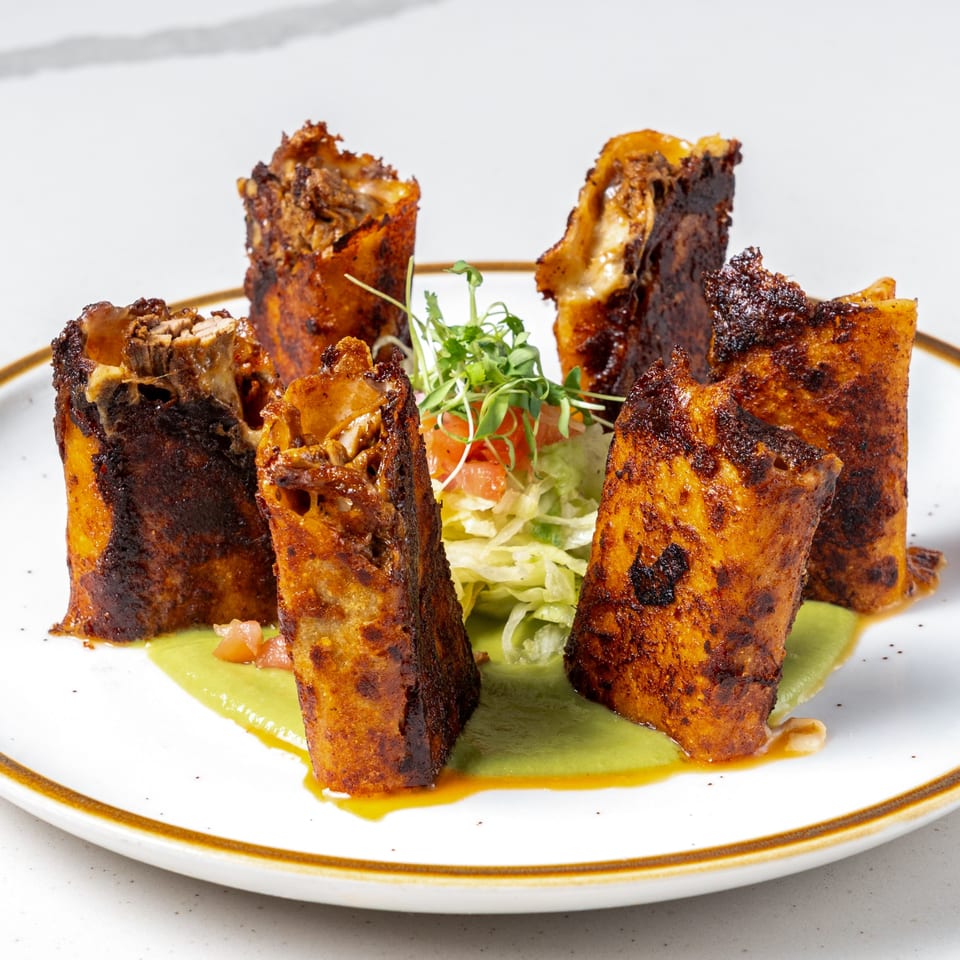 Five crispy La Prensa Tacos & Tapas taquitos stand in green sauce with a side salad.