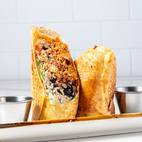 Two La Prensa Tacos & Tapas burritos, one cut open to show rice, beans, and meat, with two sauce cups.