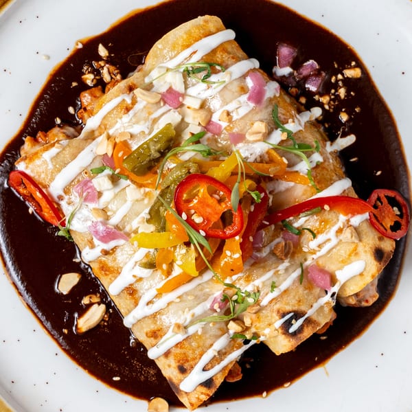 La Prensa Tacos & Tapas enchiladas with dark mole sauce, crema, peppers, and peanuts on a white plate.