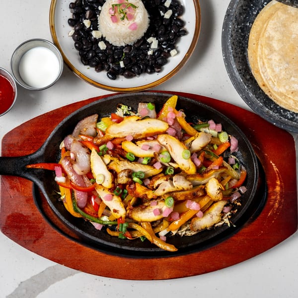 Chicken fajitas sizzling in a cast iron skillet with rice, black beans, tortillas, and sauces.