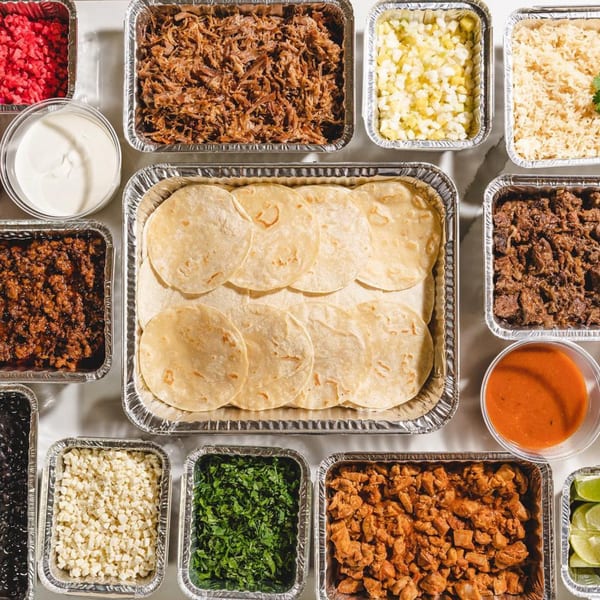 Overhead view of La Prensa Tacos & Tapas taco bar with tortillas, meats, rice, beans, and toppings.